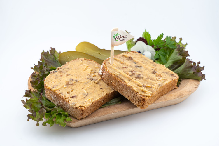 Na drewnianej desce ułożone są dwie kromki chleba razowego posmarowane grubą warstwą smalcu z dzika.