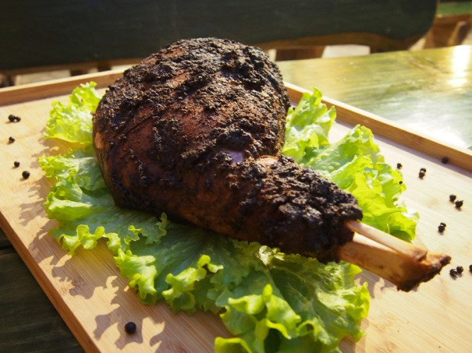 Pieczony udziec z kością leżący na liściach sałaty i drewnianej desce