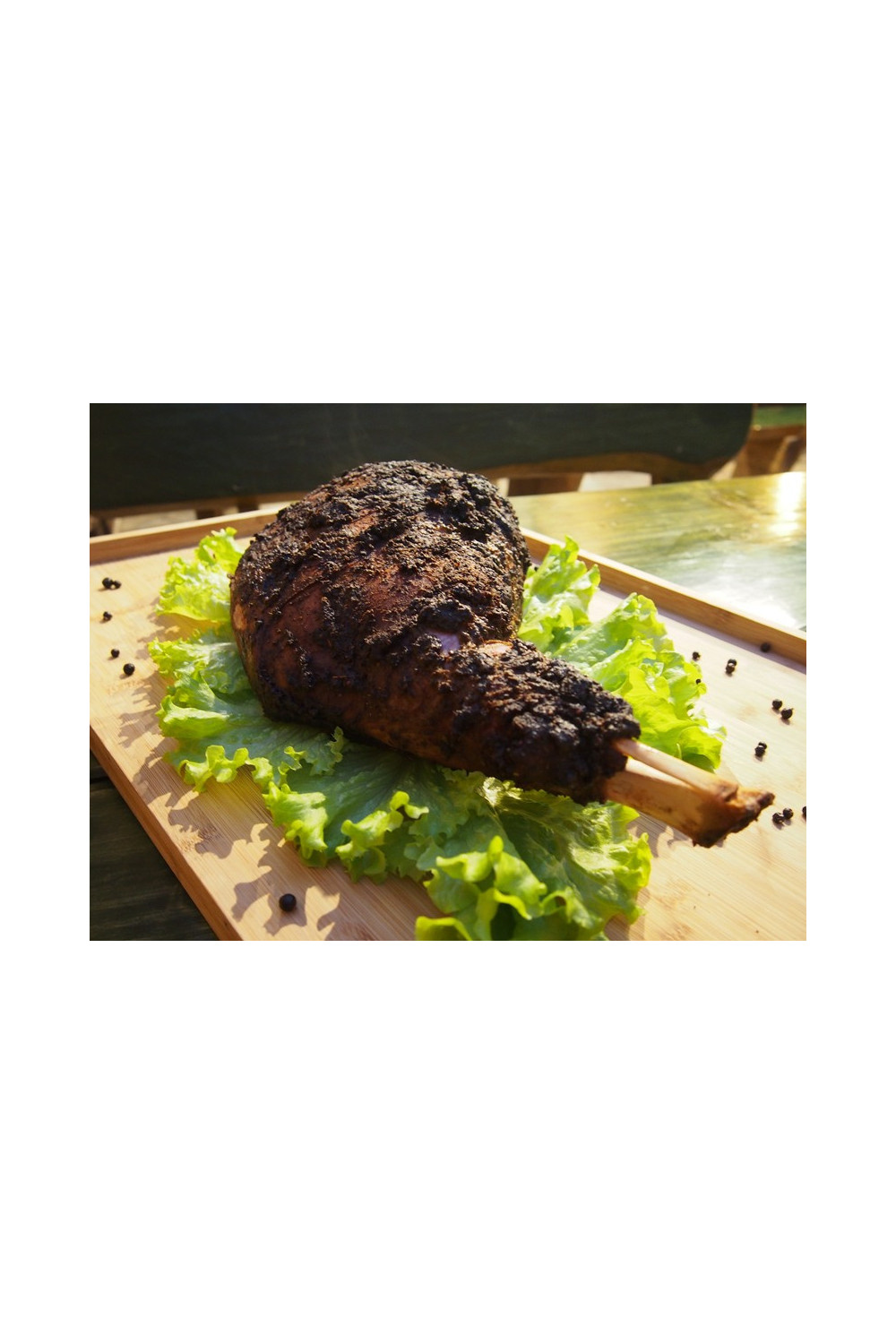 Pieczony udziec z kością leżący na liściach sałaty i drewnianej desce